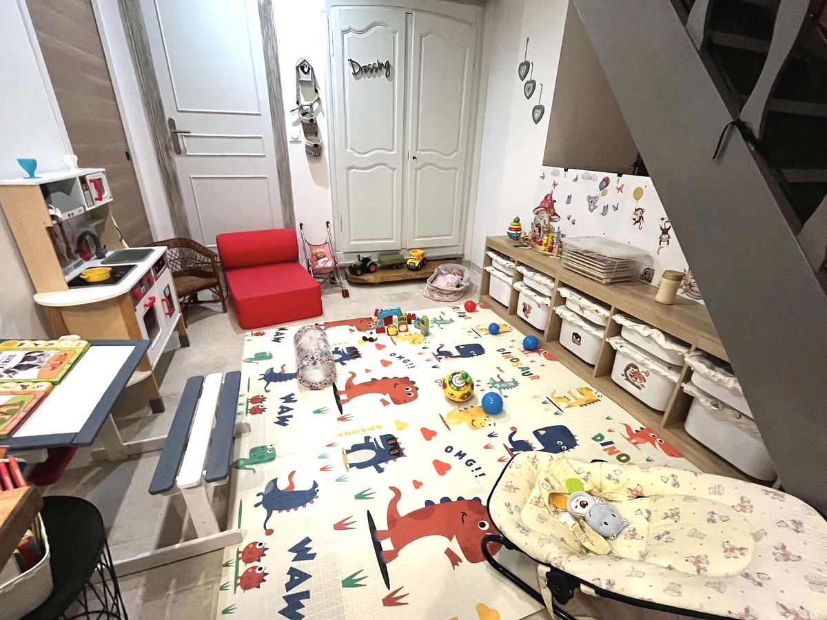 Le coin jeux aménagé pour les enfants : petite table et banc, livres, cuisine en bois, fauteuil enfant, jouets d’éveil et grand tapis de sol.