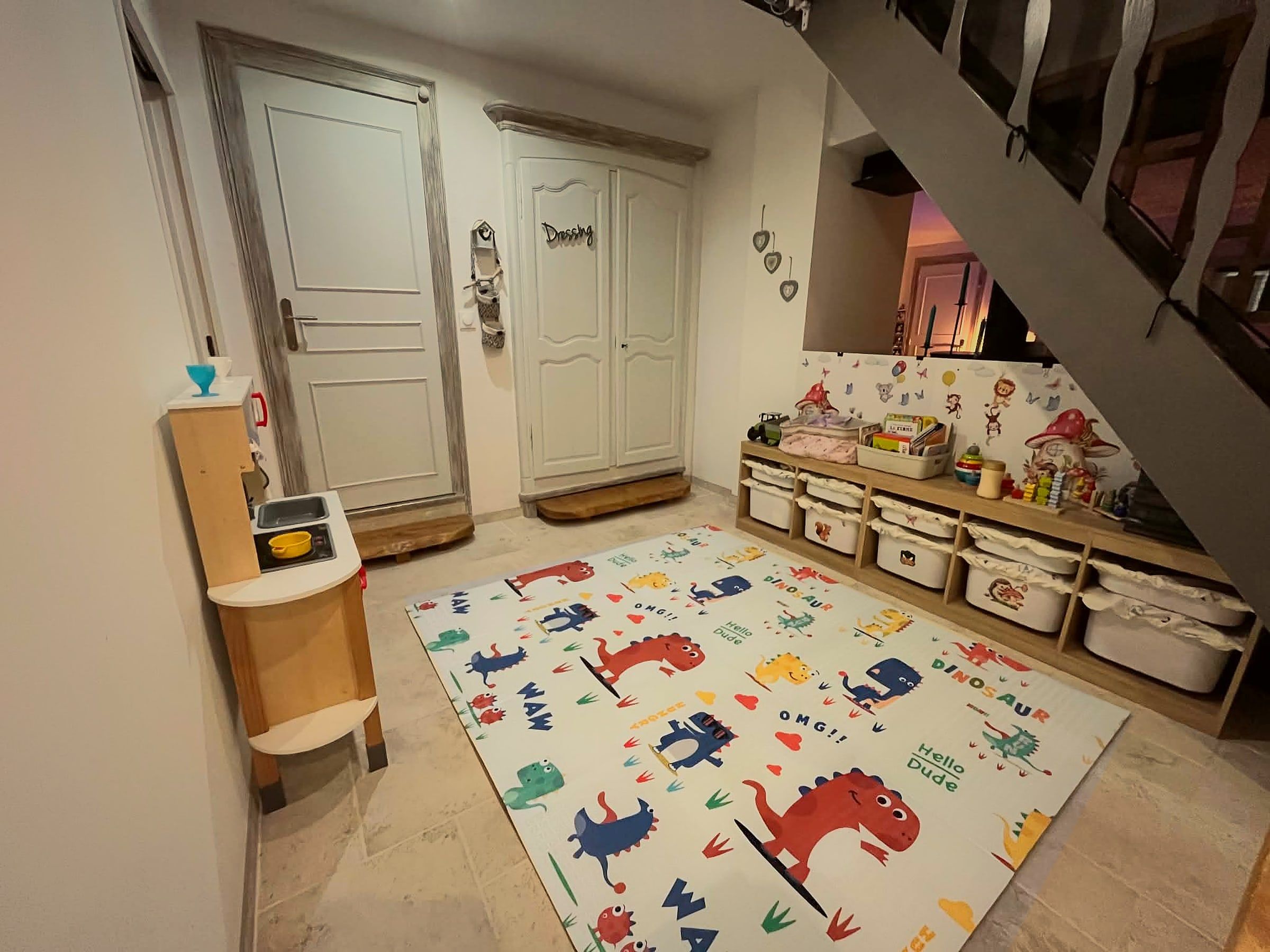 L’espace de jeu des enfants chez Catherine Herbert, assistante maternelle à Gémozac : grand tapis de sol, petite cuisine en bois et meuble de rangement avec jouets et livres.