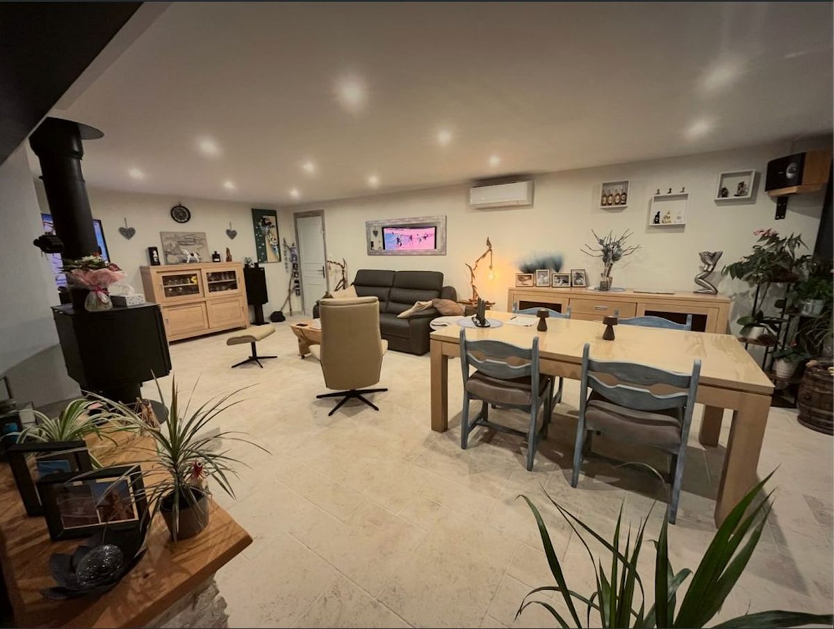 La pièce de vie lumineuse de la maison : coin salon, grande table en bois et poêle à bois.